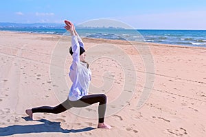 Woman does High Lunch Pose on sea sand beach yoga training sport exercise.