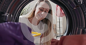 Woman does laundry, looks into washing machine, puts colored clothes inside, laundry capsule in, shot from inside drum