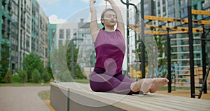 Woman does stretching and yoga exercices on the bench in the yard of an apartment building, fitness in the urban