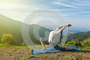 Woman does yoga asana Anjaneyasana in mountains