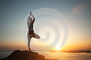 A woman does yoga and meditation on the sea beach during a beautiful sunset.