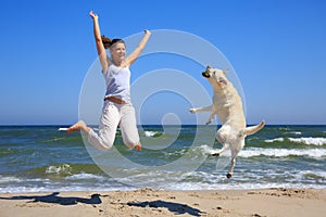 Woman and dog breed Labrador jumping on the beach