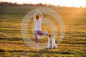 woman with dog doing yoga outdoors in beautiful sunset