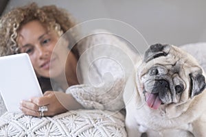 Woman and dog laying on the bed. Happy female people reding with ebook reader and having relax with her best friend old dog pug.