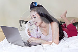 Woman and dog playing laptop on bed