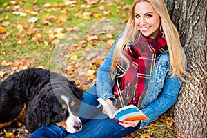 Woman with dog reading book in autumn park