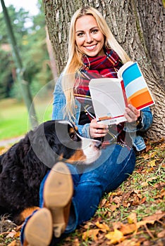 Woman with dog reading book in autumn park
