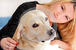 Woman with dog is resting in bed at home, relaxing in bedroom. Girl is petting with her dog. Portrait of cute yellow labrador.