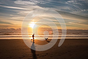 Woman and dog running free on beach on golden sunset. Fitness girl and her pet working out together