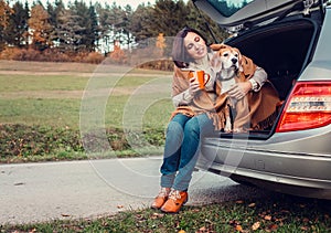 Woman with dog sit together in cat truck and warms hot tea