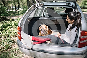 Woman and dog sitting in opened car trunk