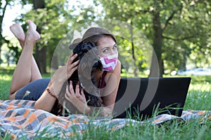 Woman with dog wearing mask and working on laptop in park