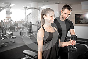 Woman doing bicep curls in gym with her personal trainer