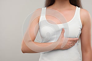 Woman doing breast self-examination on light grey background, closeup