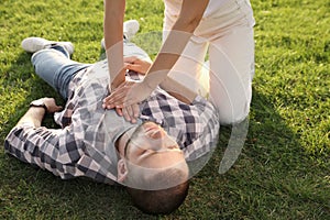 Woman doing cardiac massage to unconscious man with heart attack on green lawn