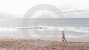 Woman is doing cardio fitness exercises on seashore. Female runner is jogging along empty sandy beach in morning. Healthy lifestyl