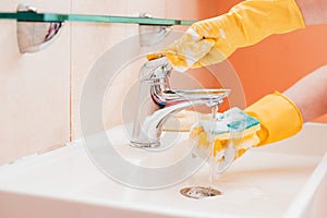 woman doing chores in bathroom at home, cleaning surfaces sink and faucet with spray detergent suds sponge.