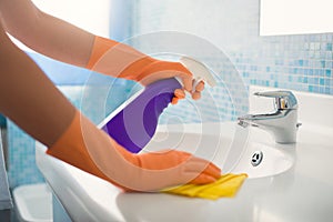 Donna che fa lavori in bagno a casa, la pulizia lavello e rubinetto, con spruzzare il detergente.