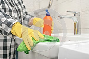 Woman doing chores cleaning bathroom at home. Cropped view of woman in rubber gloves wet rag and detergent washing sink in