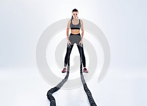 Woman doing exercises with battle rope. Photo of muscular model in sportswear isolated on white background