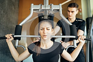Woman doing fitness exercises on home gym lat pull down machine with personal trainer.Making an effort and training hard for fit