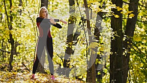 Woman doing fitness exercises outdoor. Female stretching her shoulders in autumn forest. Slim girl at work-out - the left side