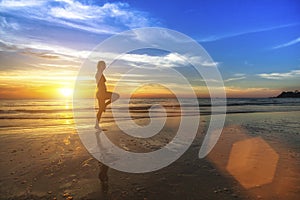 Woman doing fitness on the ocean beach during the amazing sunset.