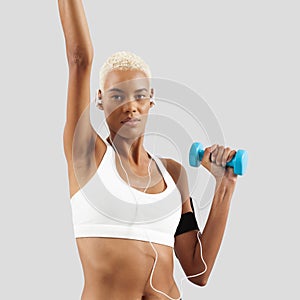 woman doing fitness workout, lifts dumbbells while listening music through earphones of mobile phone on arm band. Latin American