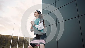 Woman doing fitness workout outdoor with rubber resistance band. Sportswoman in sporty leggings and top makes squats