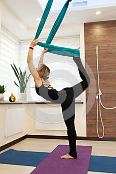 Woman doing fly yoga stretching standing on one leg on the ground and second in hammock. Fit and wellness lifestyle