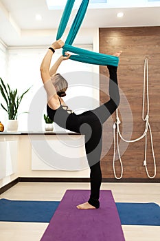 Woman doing fly yoga stretching standing on one leg on the ground and second in hammock. Fit and wellness lifestyle