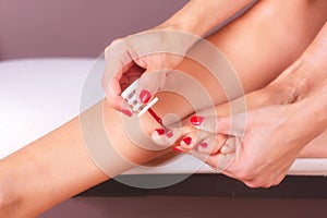 Woman doing foot care and nail treatment. Applying red nail polish.