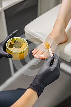 Woman doing foot peeling in pedicure SPA salon. Sugar scrub and relax beauty procedure