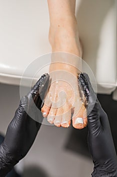 Woman doing foot peeling in pedicure SPA salon. Sugar scrub and relax beauty procedure