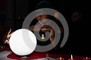 Woman doing fortune telling witchcraft forecasting the future with crystal ball and Tarot card on red table