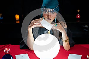 Woman doing fortune telling witchcraft forecasting the future with crystal ball and Tarot card on red table