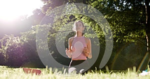 Woman doing hands and meditation pose for yoga practice surrounded by green park, forest, and big tree. Woman enjoy yoga