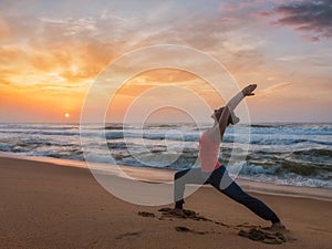 Woman doing yoga asana Virabhadrasana 1 Warrior Pose on beach on