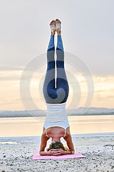 Woman doing Hatha yoga headstand or Sirsasana on nature rear view