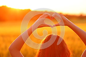 Woman doing heart shape in a field at sunset