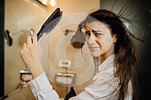 Woman doing her hair styling with a brush at home.Bad hair day.Daily hairstyle preparation routine.Heat damage,split ends,dry hair