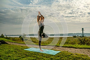 Woman doing her morning yoga in the park under sunrise, in Vrikshasana or Tree pose