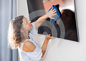 Woman doing housework - washing TV screen with dishcloth