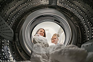 Woman Doing Laundry with her daughter Reaching towel Inside Washing Machine