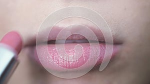 Woman doing make up lips paints pink lipstick on top her lips