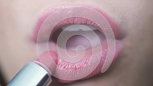 Woman doing make up lips paints pink lipstick on top her lips. Close up