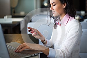 Woman doing online shopping at cafe, holding credit card typing numbers on laptop computer side view