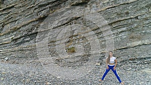 Woman is doing plie squats the bodyflex during breathing exercises on the rock background. Aerial beautiful footage view