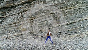 Woman is doing plie squats the bodyflex on the rock and sea background. Aerial beautiful footage view.