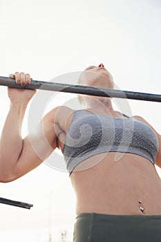 Woman doing pull up exercise on bar against clear sky
